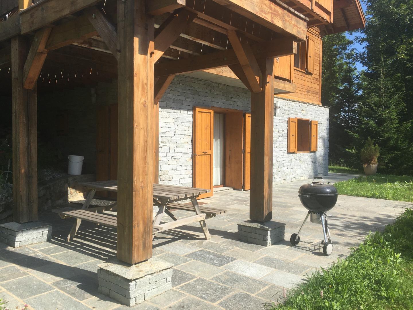 Le chalet en été avec sa terrasse privative, table et barbecue.